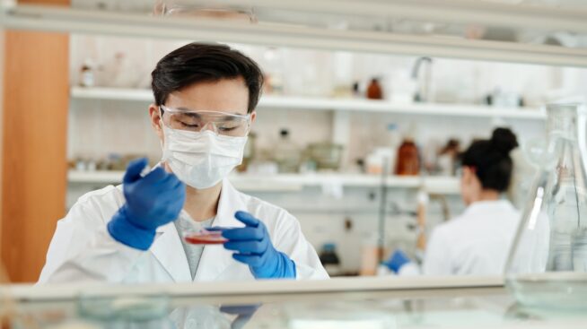 Masked laboratory worker dispensing blood sample on a petri dish