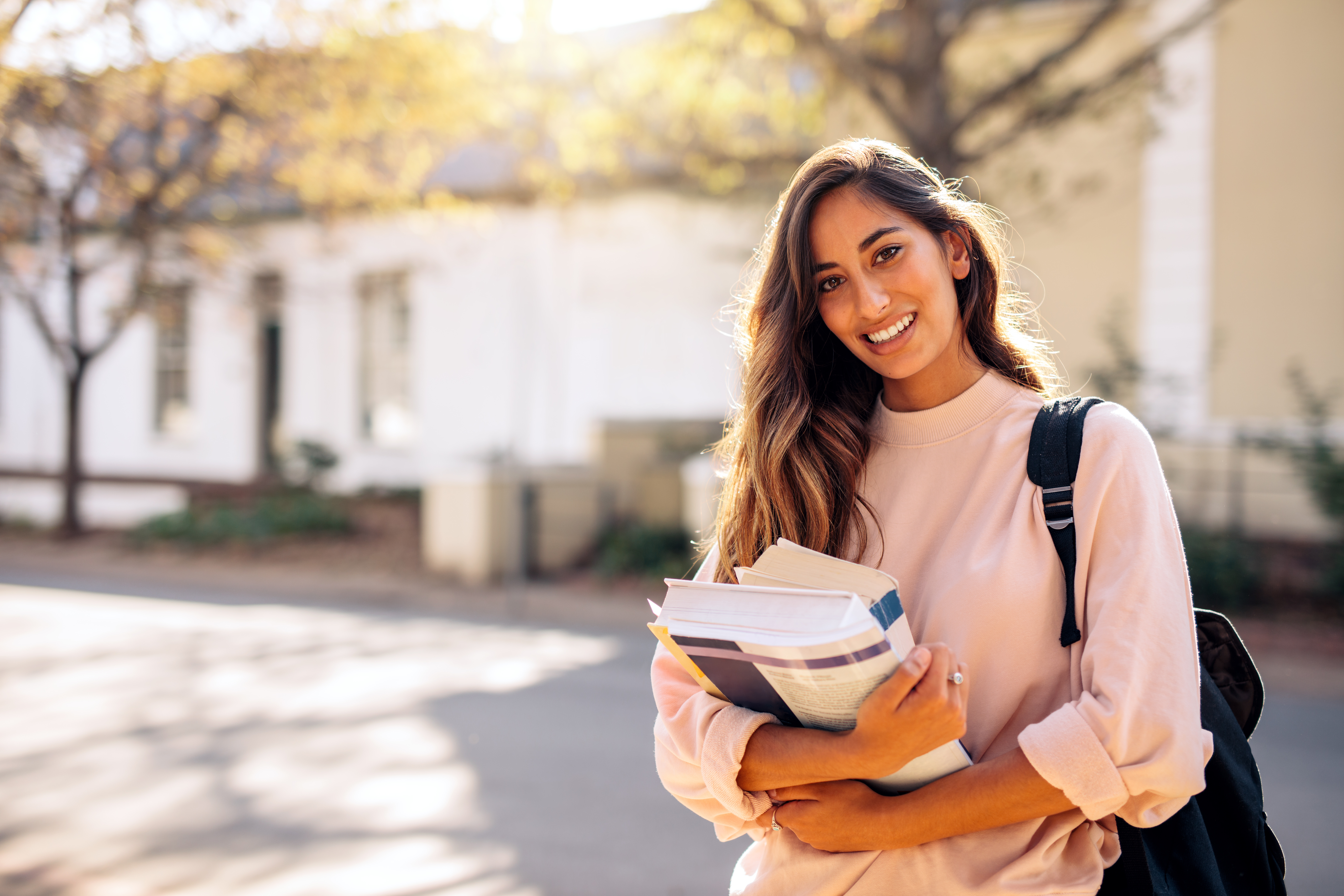 Female college student smiling while holding books.