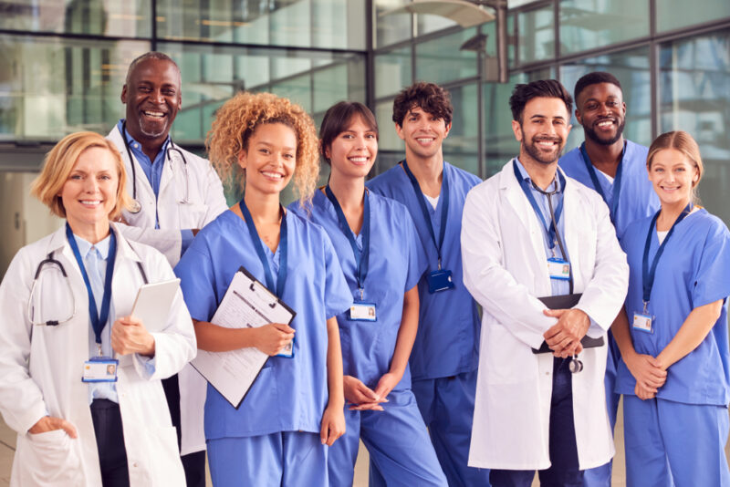 Group of smiling multi-ethnic medical faculty and research professionals standing in front of a building