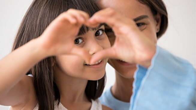 Mother and daughter with daughter peering through a heart formed by her hands.
