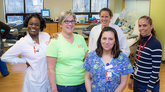 Diverse group of five smiling Rhode Island Blood Center staff members in a blood donation center.