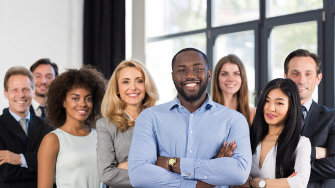 Diverse group of eight colleagues smiling in an office environment.