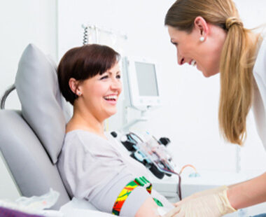 Smiling middle-aged woman donating blood at a Rhode Island Blood Center with smiling phlebotomist attending to her.
