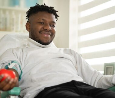 A smiling man with a red foam ball in his hand donating blood.