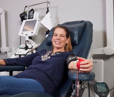 Smiling blood donor squeezing foam red heart in donation chair