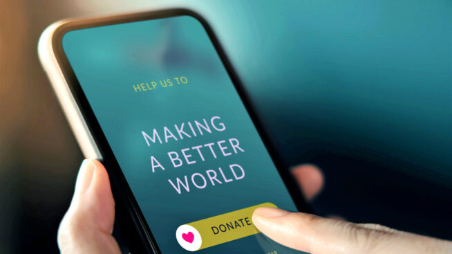 Person holding a mobile phone making an online donation. Phone screen reads, Making a Better World. Peron's finger is pointing to a swipe image that reads, Donate, with a heart image.