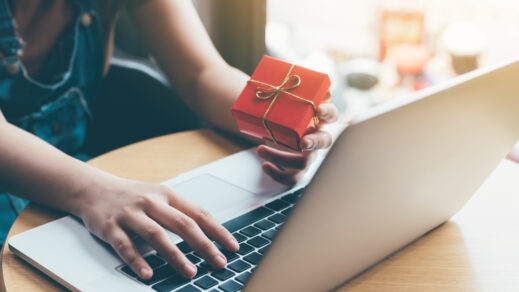 Woman at her laptop holding a red gift box as she shops online.
