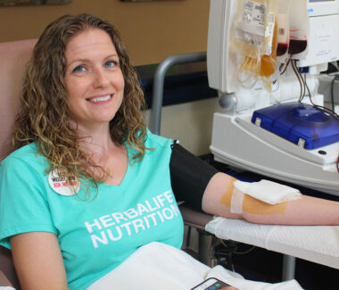 Female blood donor giving blood at a Delmarva blood donation location while smiling at the camera.