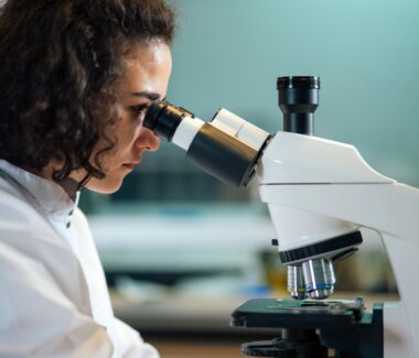 Female research scientist peering into microscope on a desk