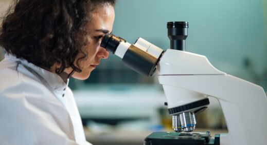 Female research scientist peering into microscope on a desk