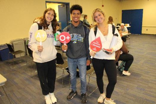 Three University of Delaware students holding up signs displaying their blood types.