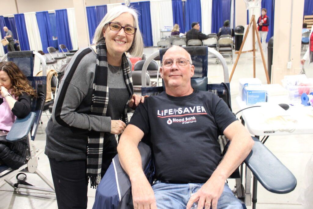Smiling couple as man is in donation chair preparing to give blood.