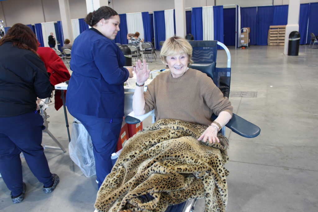 A smiling blood donor with a leopard print blanket over her lets.