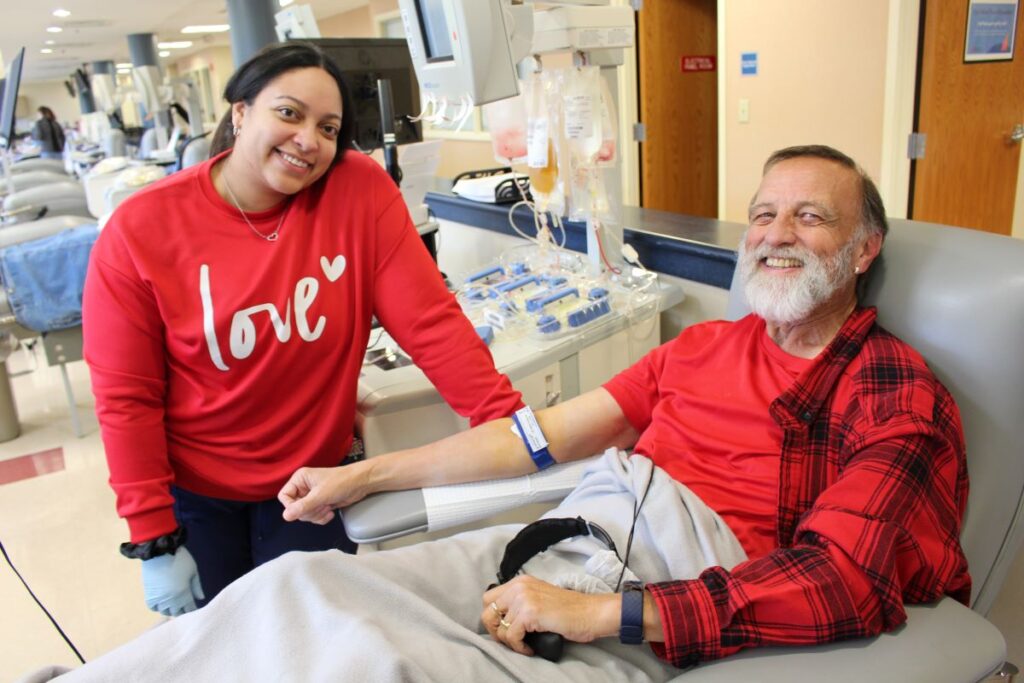 Smiling blood donor with a BBD staff member wearing a red sweatshirt reading Love.