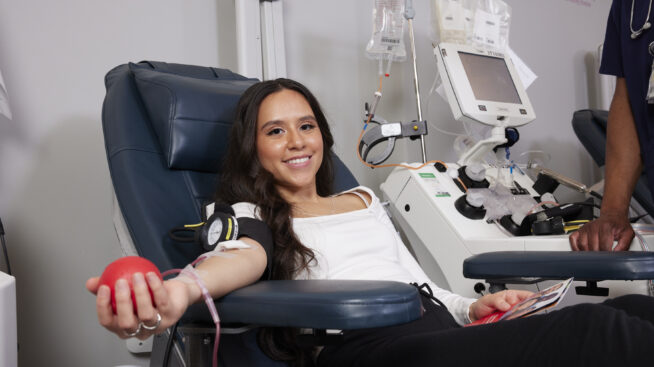 Smiling blood donor in donation chair squeezing a red foam heart.