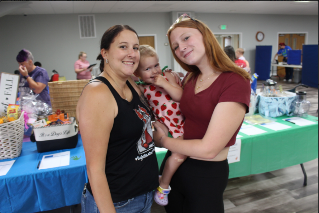Two smiling blood donors posing with a baby at a BBD blood drive.