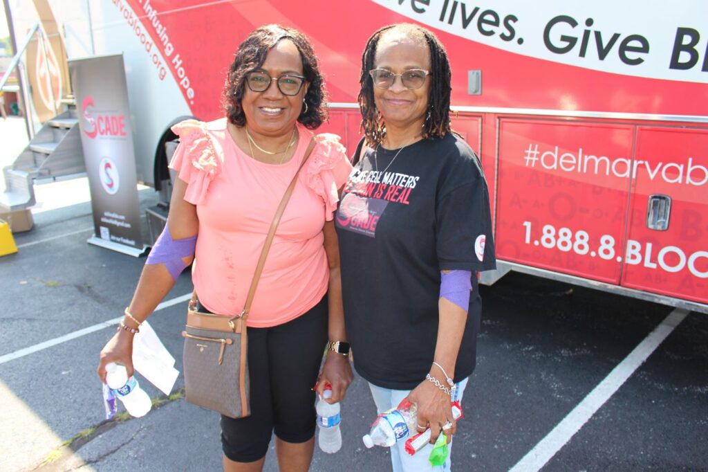 Two blood donors smiling in front of the BBD blood drive bus.