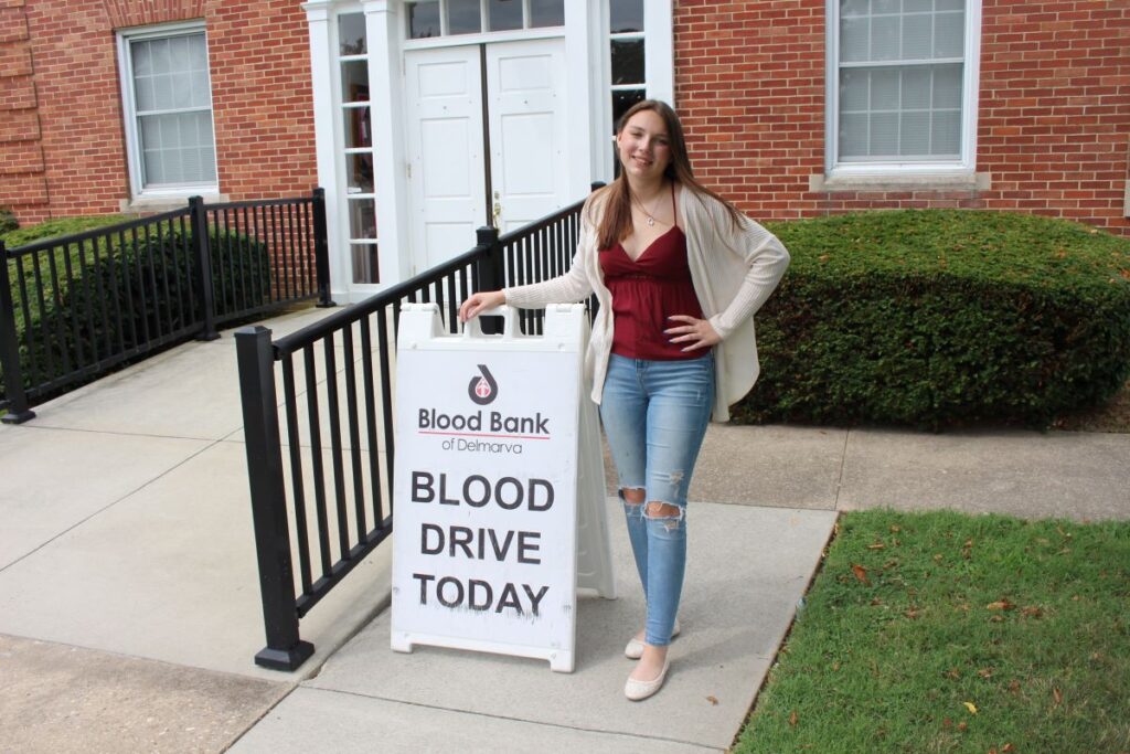 Faith Hubbard standing next to sign reading "Blood Drive Today."