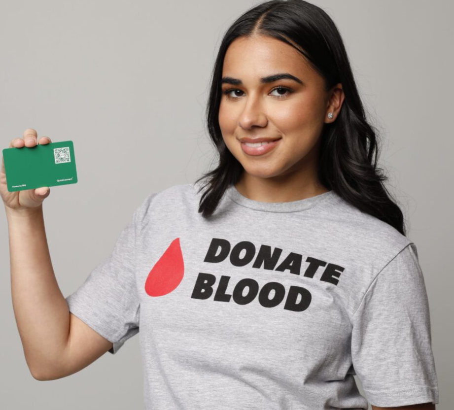 Smiling woman wearing a Donate Blood tshirt holding up her donation registration card.