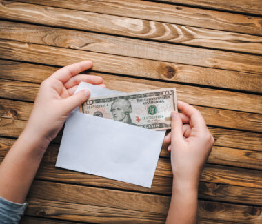 Hands putting money into an open envelope on a table.