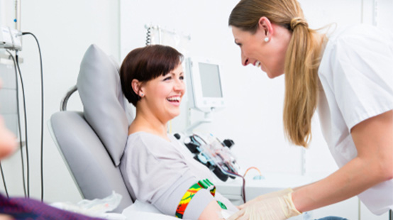A smiling woman in a donation chair being prepared for a blood donation by a MBC phlebotomist.