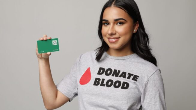 Blood donor wearing a tshirt that reads Donate Blood holding a Loyalty Rewards Card.